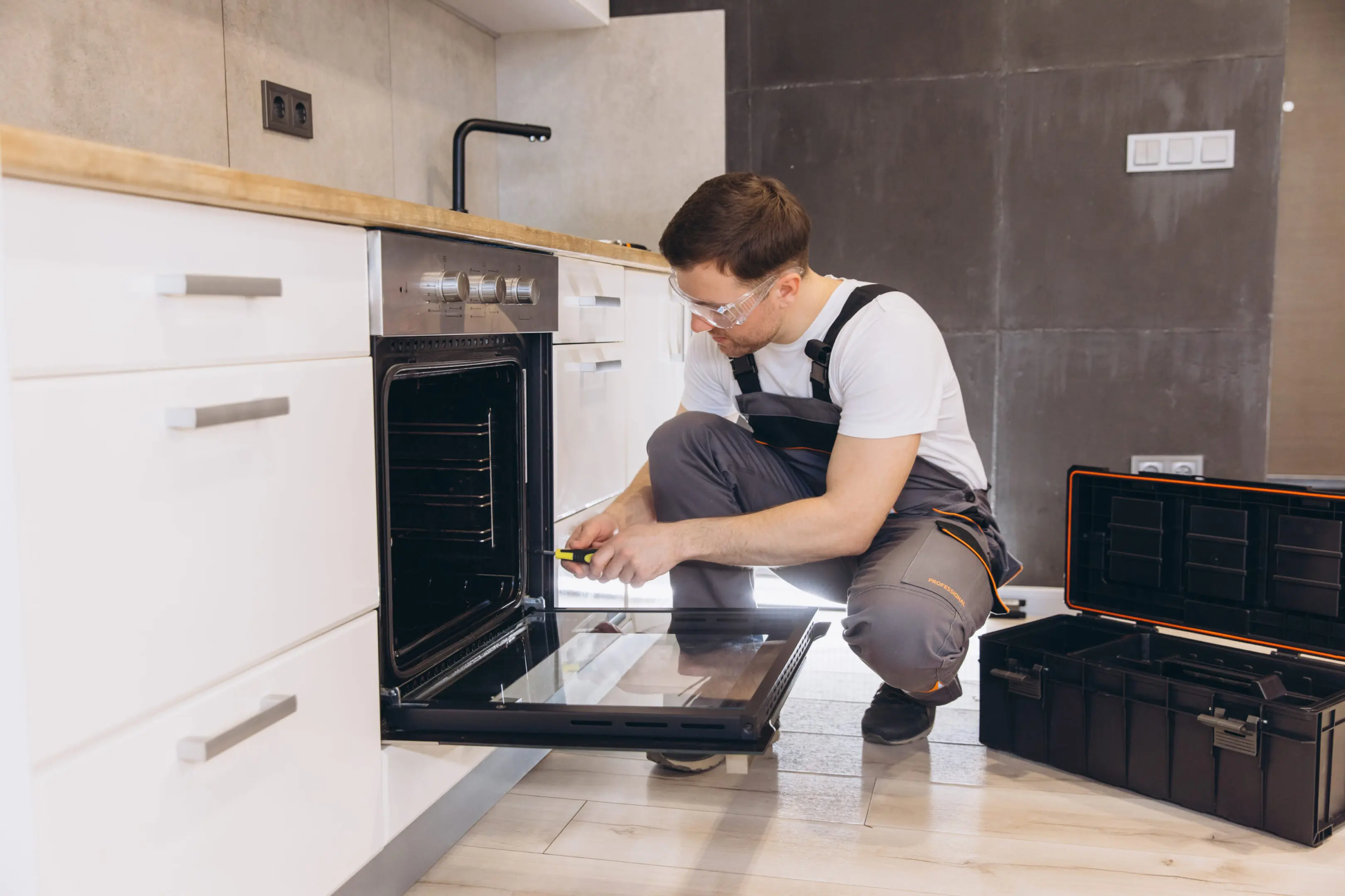 Professional plumber repairing oven in a modern kitchen A man kneeling down in front of an oven.