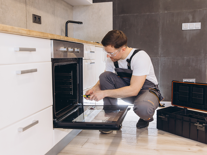 A man in an apron is fixing the oven.
