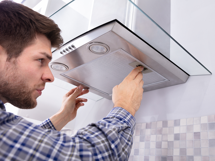 A man is fixing the exhaust fan on the wall.