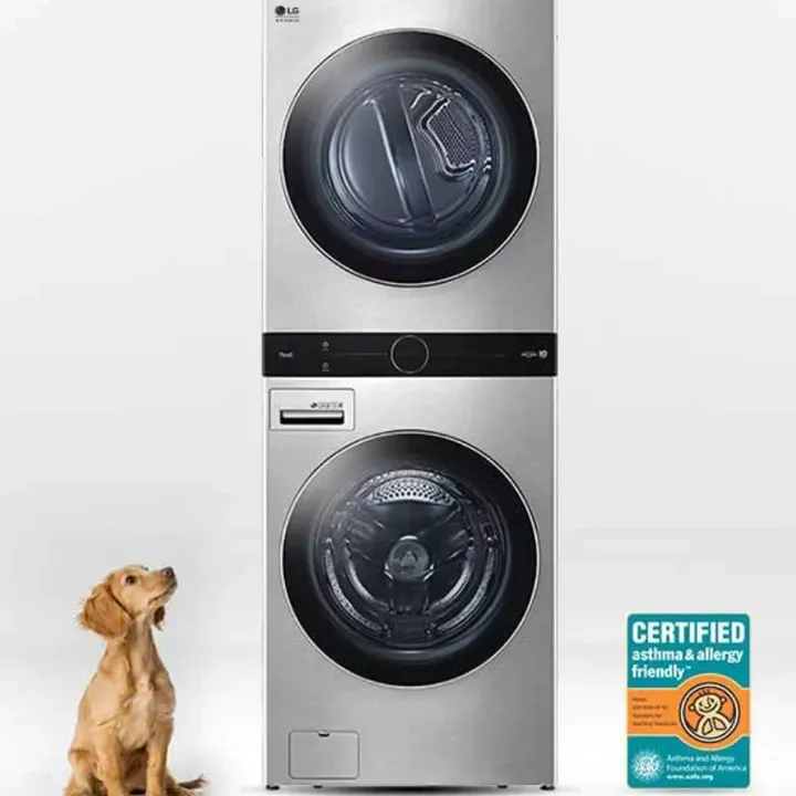 A dog sitting next to two stacked washer and dryer.